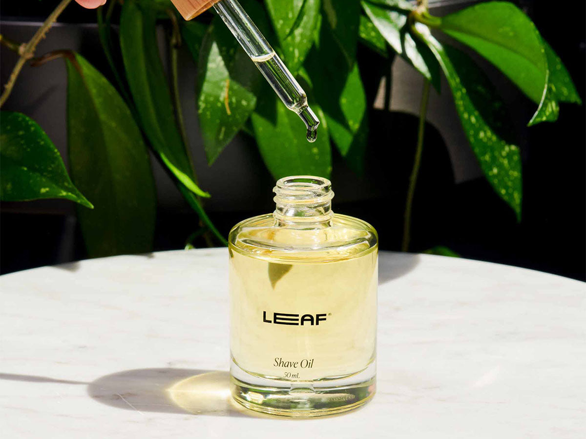 Glass bottle of leaf shave oil, on a marble table, with dropper above it