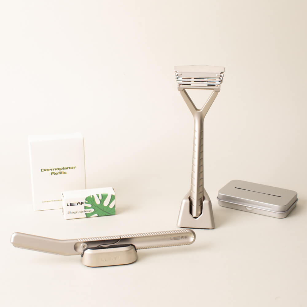 The silver full face and body kit displayed with the triple edge razor, dermaplaner, a stand and blades, for each, and the recycling tin