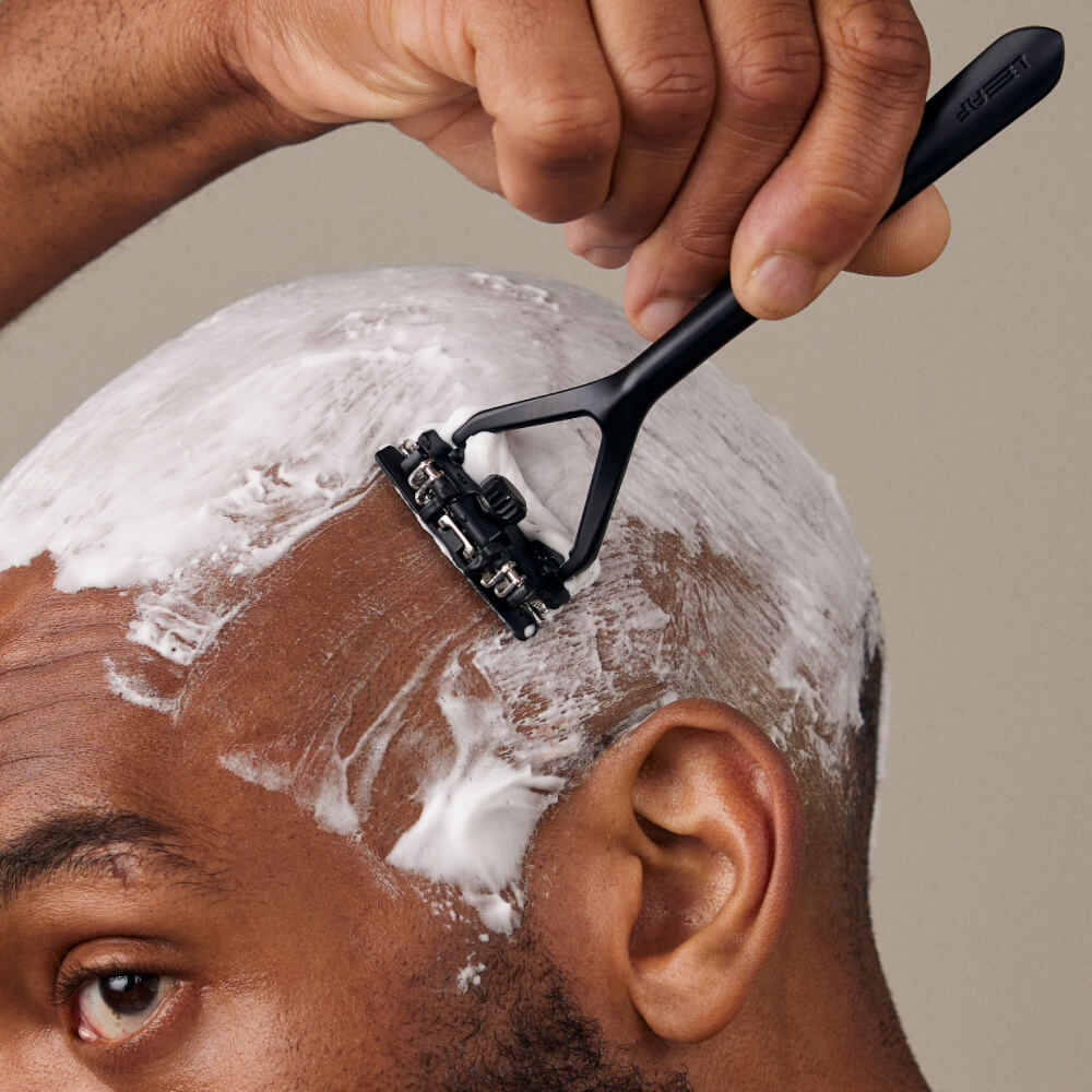 Man shaves his head covered in shave soap with a Leaf razor